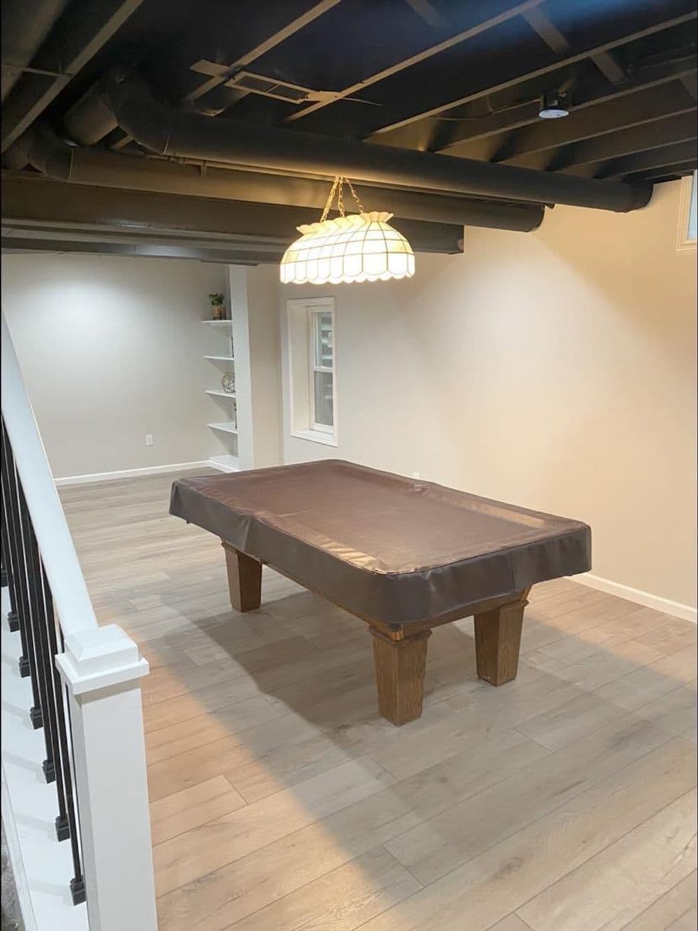 Finished basement with a billiard table and modern lighting. Warm wooden flooring enhances the space.