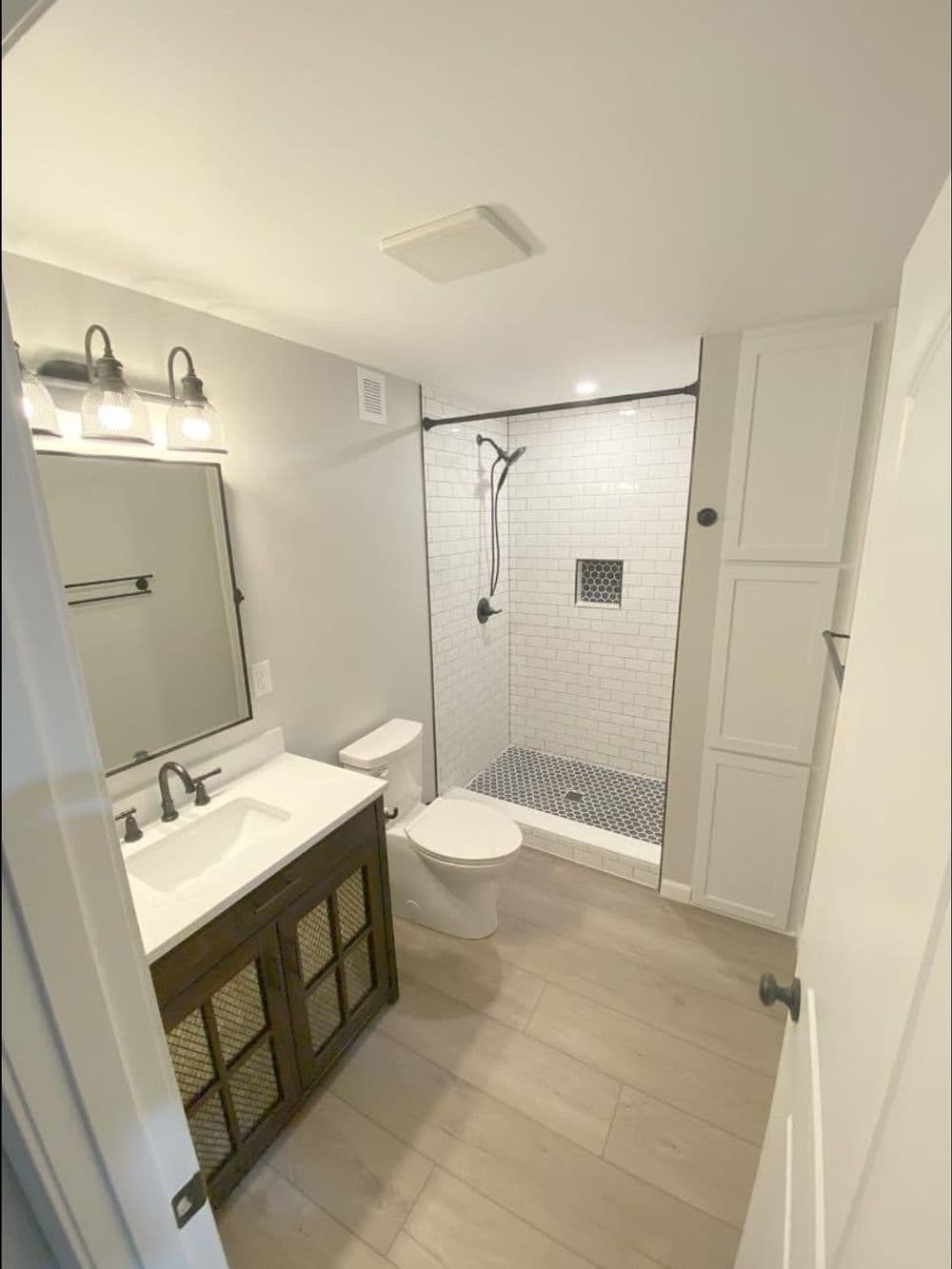 Modern bathroom with shower, white tile, wooden vanity, and stylish lighting.