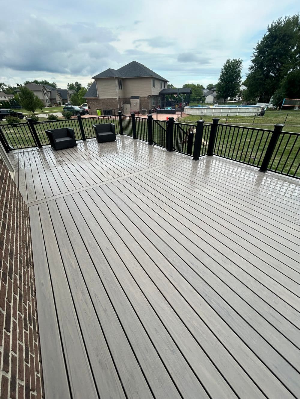Spacious composite deck with black railings and two chairs overlooking a backyard.