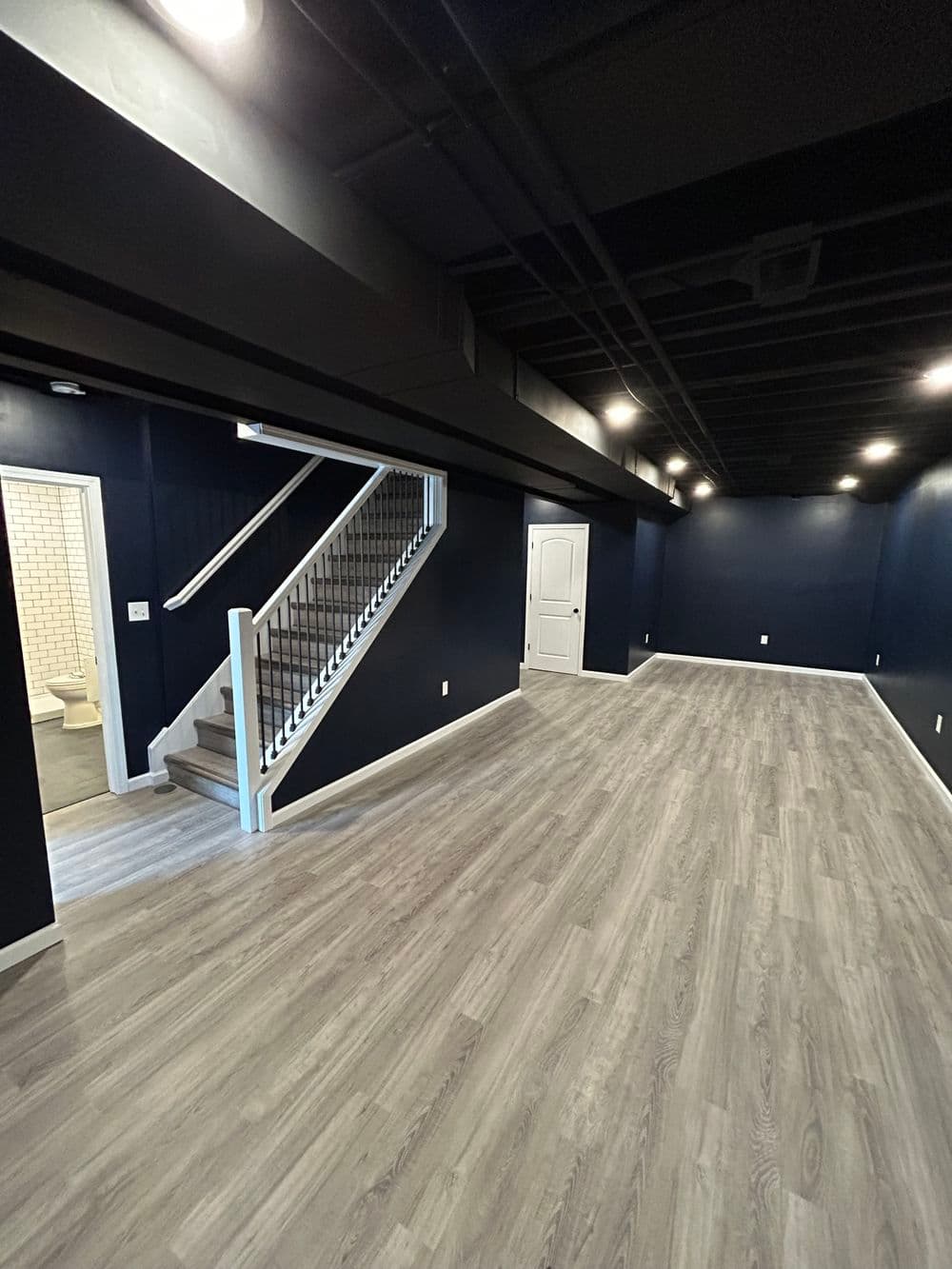 Spacious modern basement with dark walls, wooden floors, and staircase access.