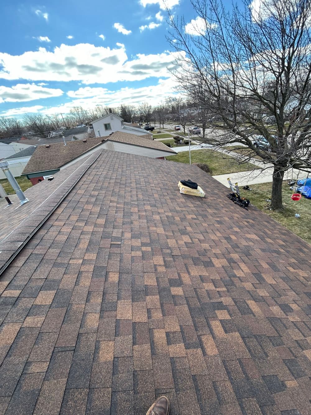 Aerial view of a residential roof with new shingles under a partly cloudy sky.