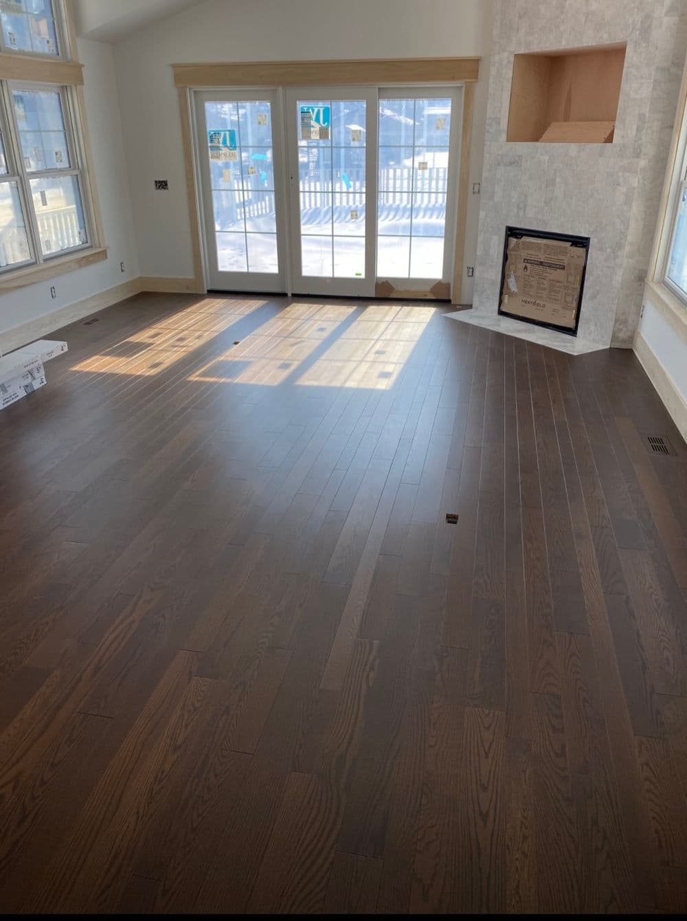 Spacious room with dark hardwood flooring, large windows, and a modern fireplace.