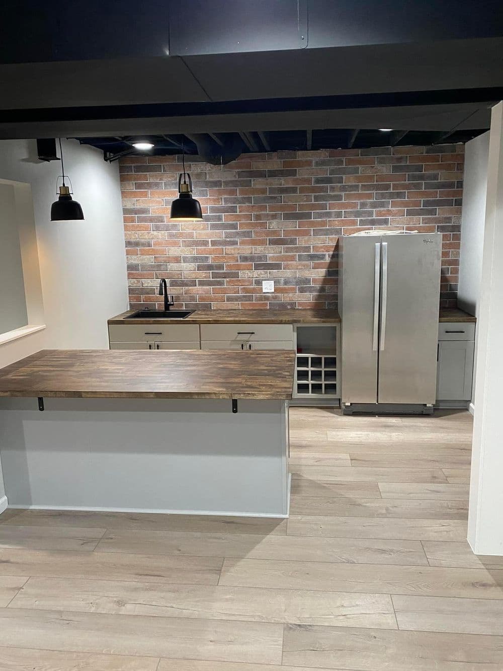 Modern kitchen with wood countertops, stainless steel fridge, and brick accent wall.