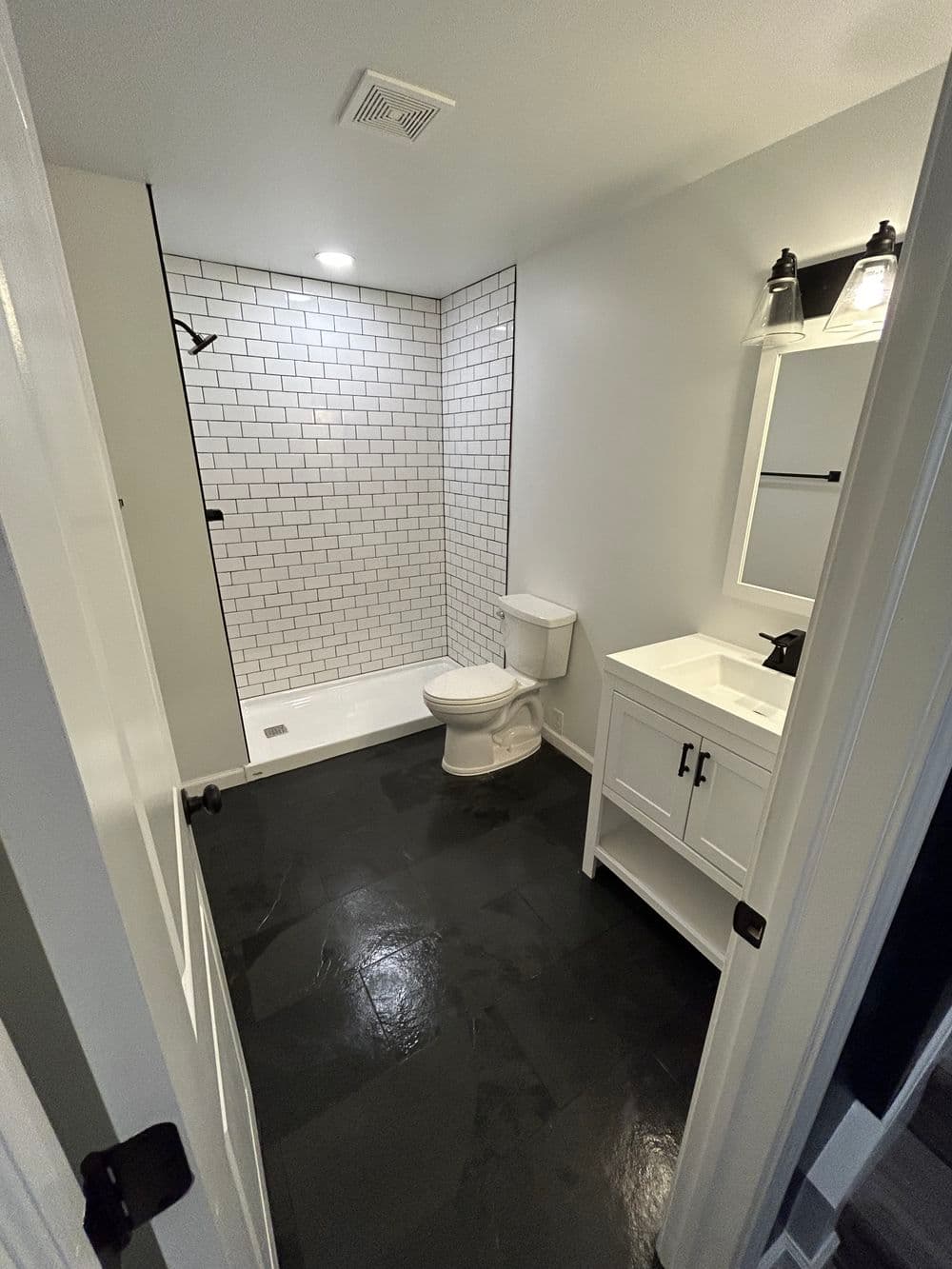 Modern bathroom with white subway tile shower, black slate floor, and stylish vanity.