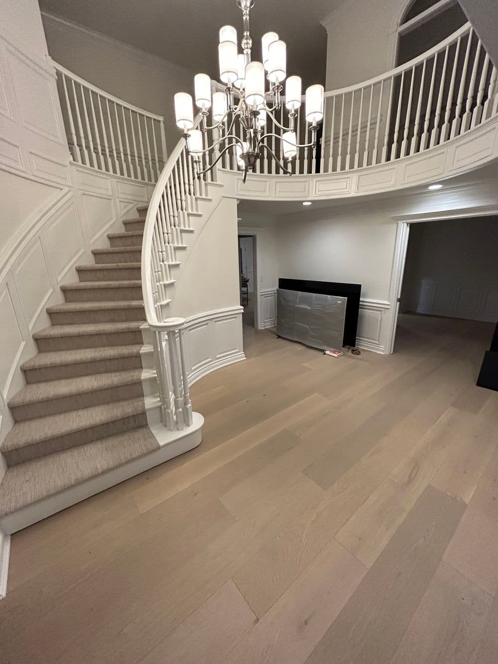 Elegant foyer with curved staircase, modern chandelier, and light wood flooring.
