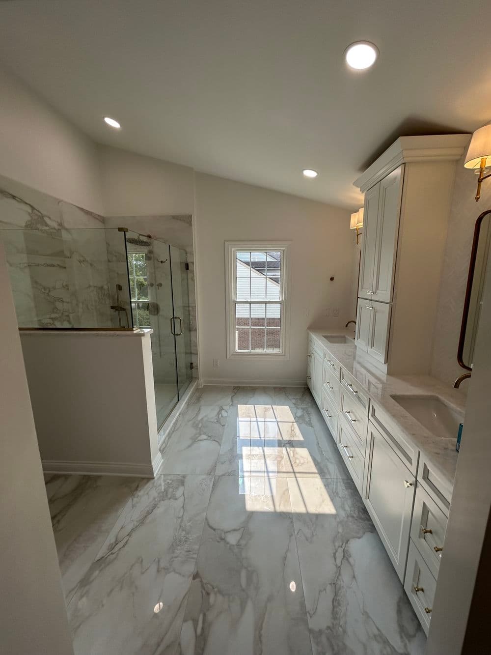 Modern bathroom with marble flooring, glass shower, and elegant cabinetry, bright natural light.