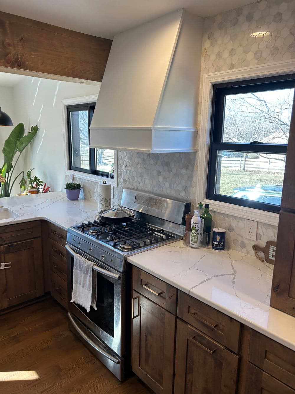 Modern kitchen with stainless steel range hood, natural wood cabinets, and marble countertops.